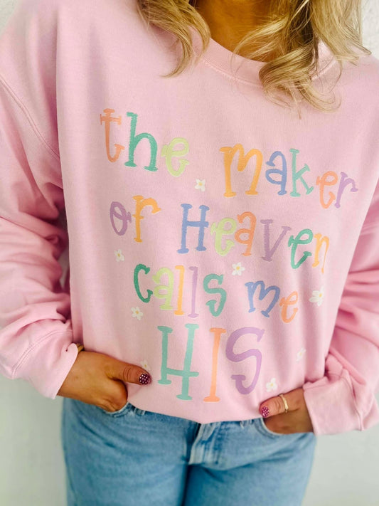 Person wearing a pink sweatshirt with colorful text design, the maker of heaven calls me HIS, standing against a plain background.