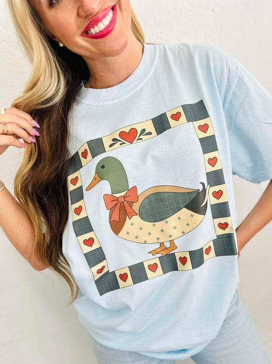 Woman wearing a light blue t-shirt with a duck mallard patchwork graphic design.