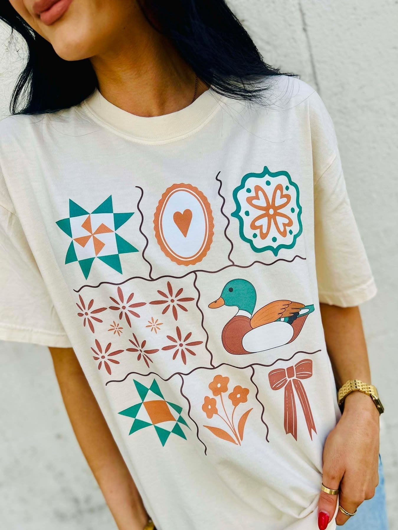 Person wearing a white t-shirt with colorful Antique Designs patterns and a mallard duck illustration.