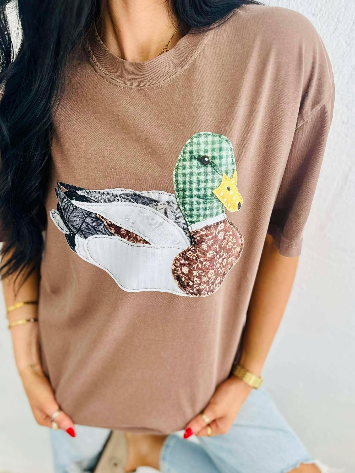 Person wearing a brown t-shirt with a viral patchwork mallard duck graphic design.