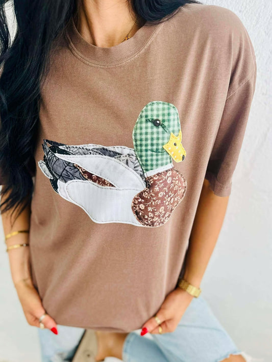 Person wearing a brown t-shirt with a viral patchwork mallard duck graphic design.