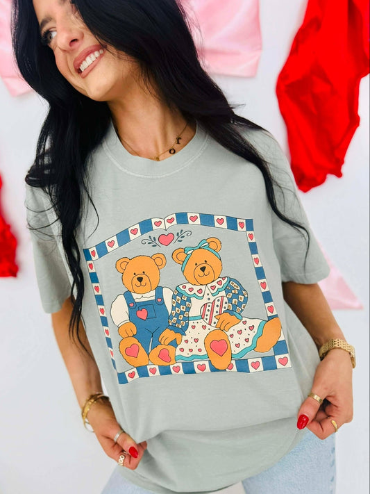 Woman wearing a light gray t-shirt with teddy bear design, standing against a colorful background.