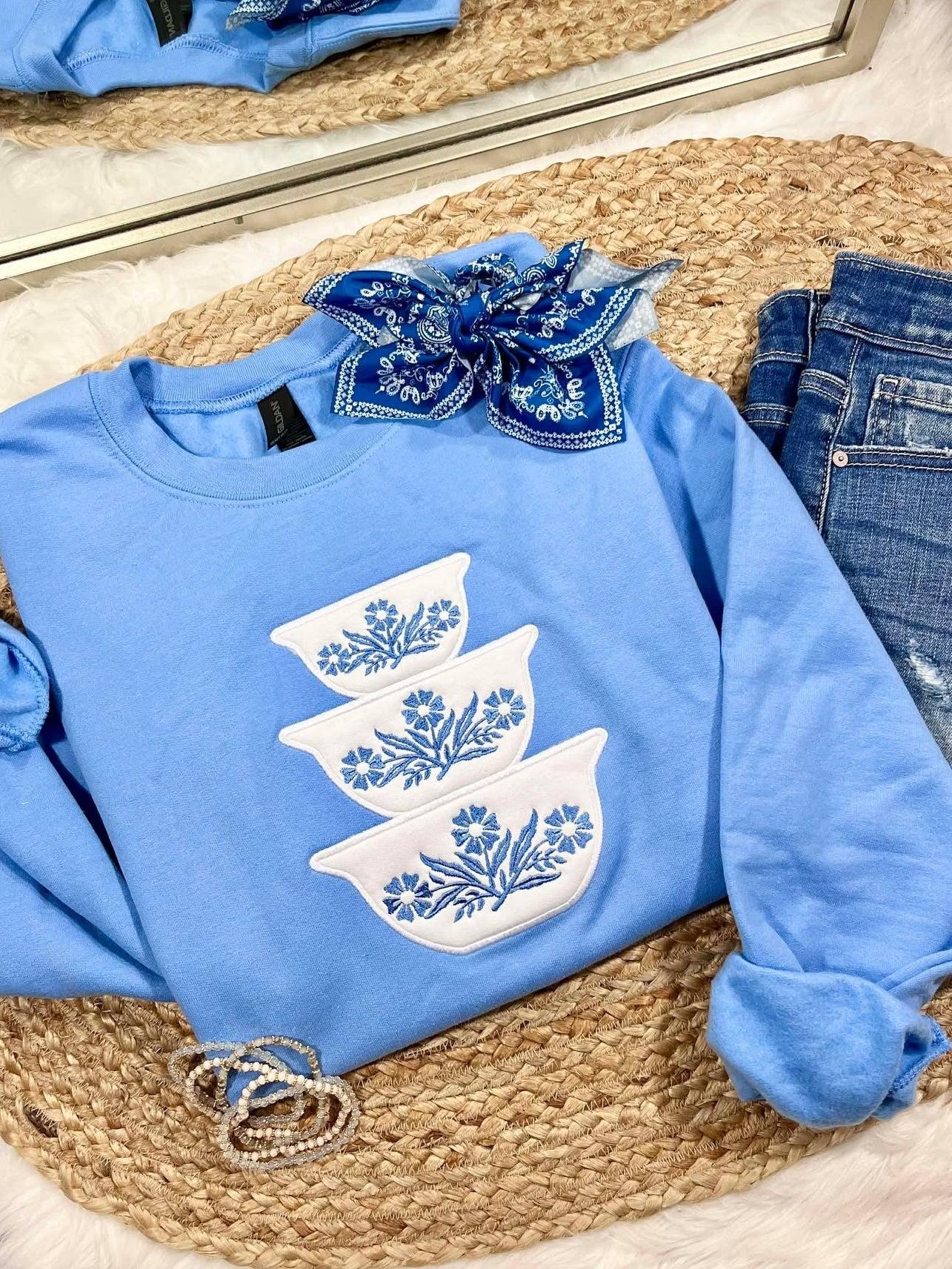 Blue sweatshirt with white floral designs on a woven mat