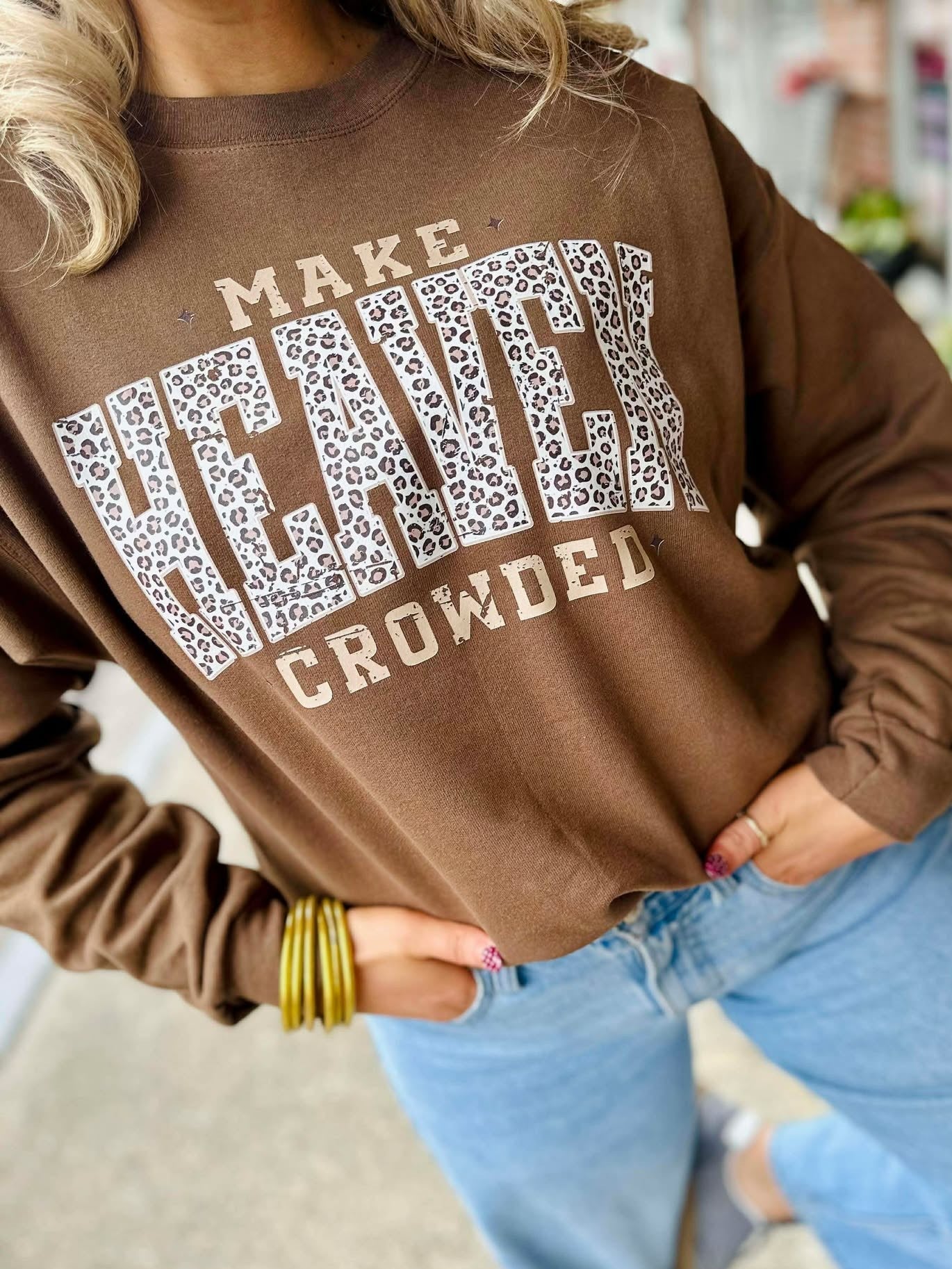 Person wearing a brown sweatshirt with text and leopard print design, standing on a sidewalk.