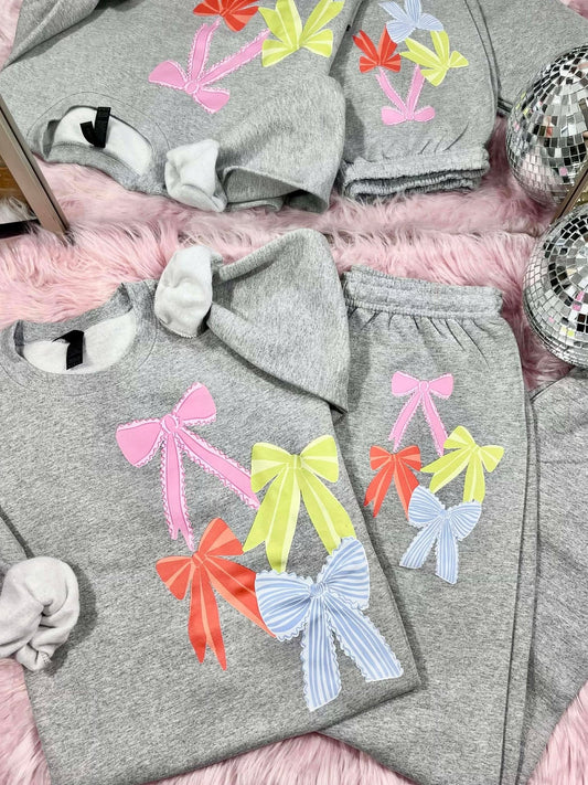 Gray sweatshirt and pants set with colorful bows on a pink surface.