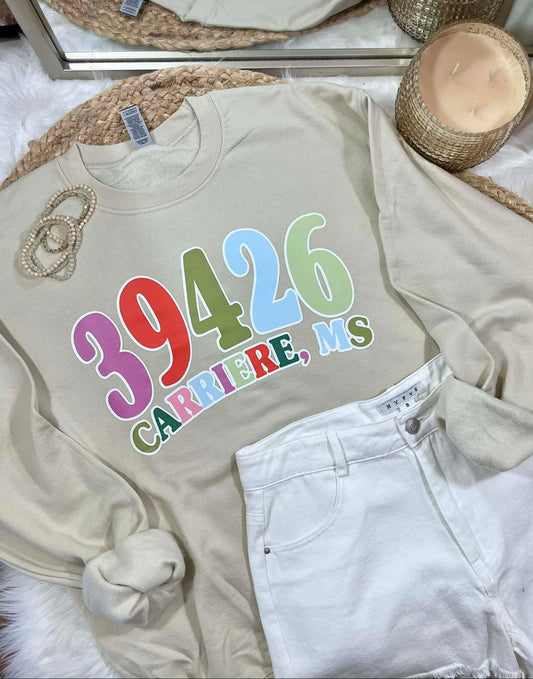 Beige sweatshirt with colorful zipcode  text on a bed