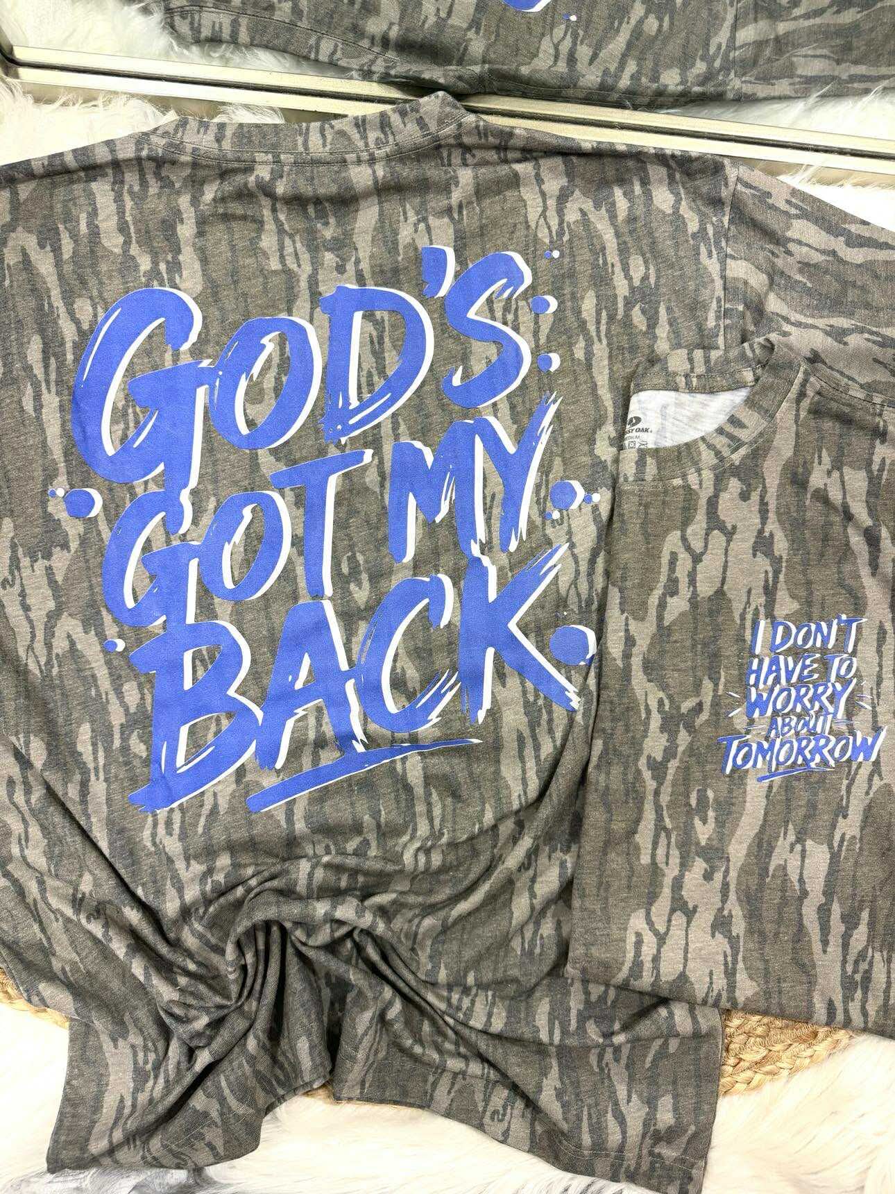 Mossy Oak Bottomland t-shirt with blue text 'God's Got My Back' on a white background