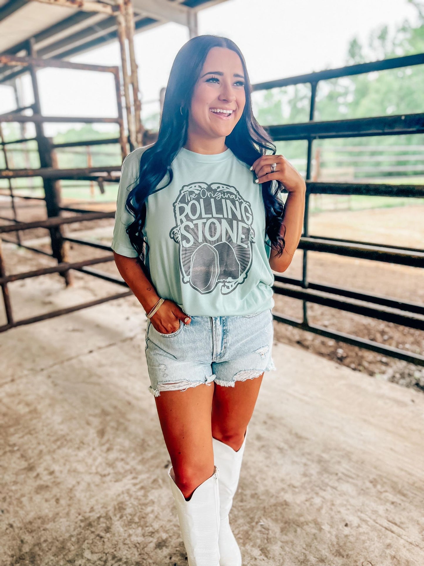 A person standing in an outdoor setting wearing a blue t-shirt with 'Rolling Stones' text and a graphic of a stone on it, paired with denim shorts.