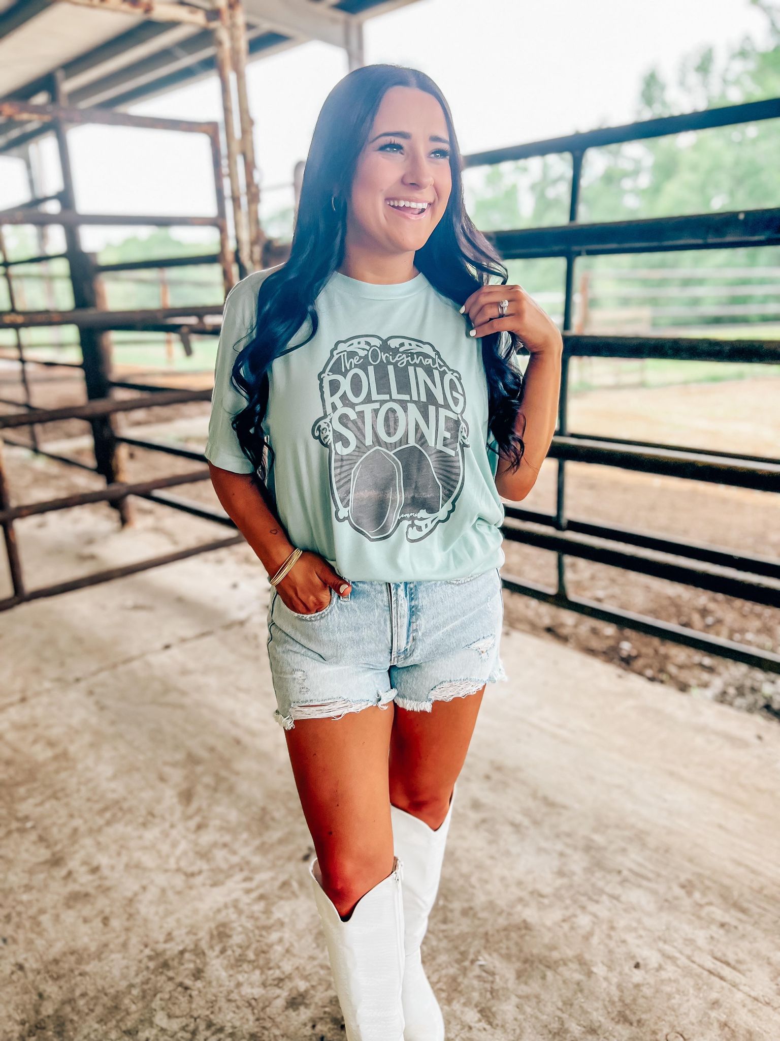 A person standing in an outdoor setting wearing a blue t-shirt with 'Rolling Stones' text and a graphic of a stone on it, paired with denim shorts.