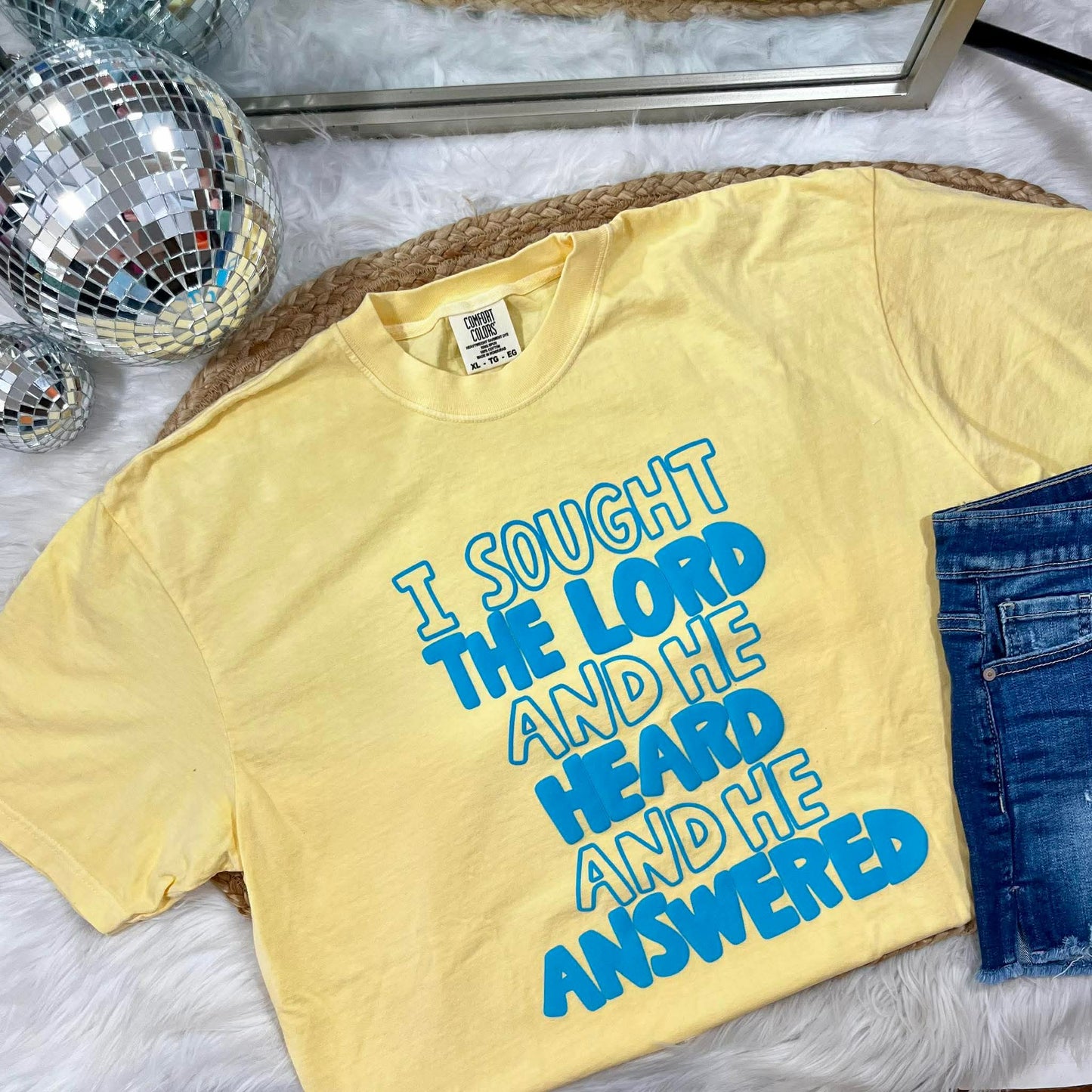 Yellow t-shirt with blue Puff vinyl 'I SOUGHT THE LORD AND HE HEARD AND HE ANSWERED' on a textured surface.