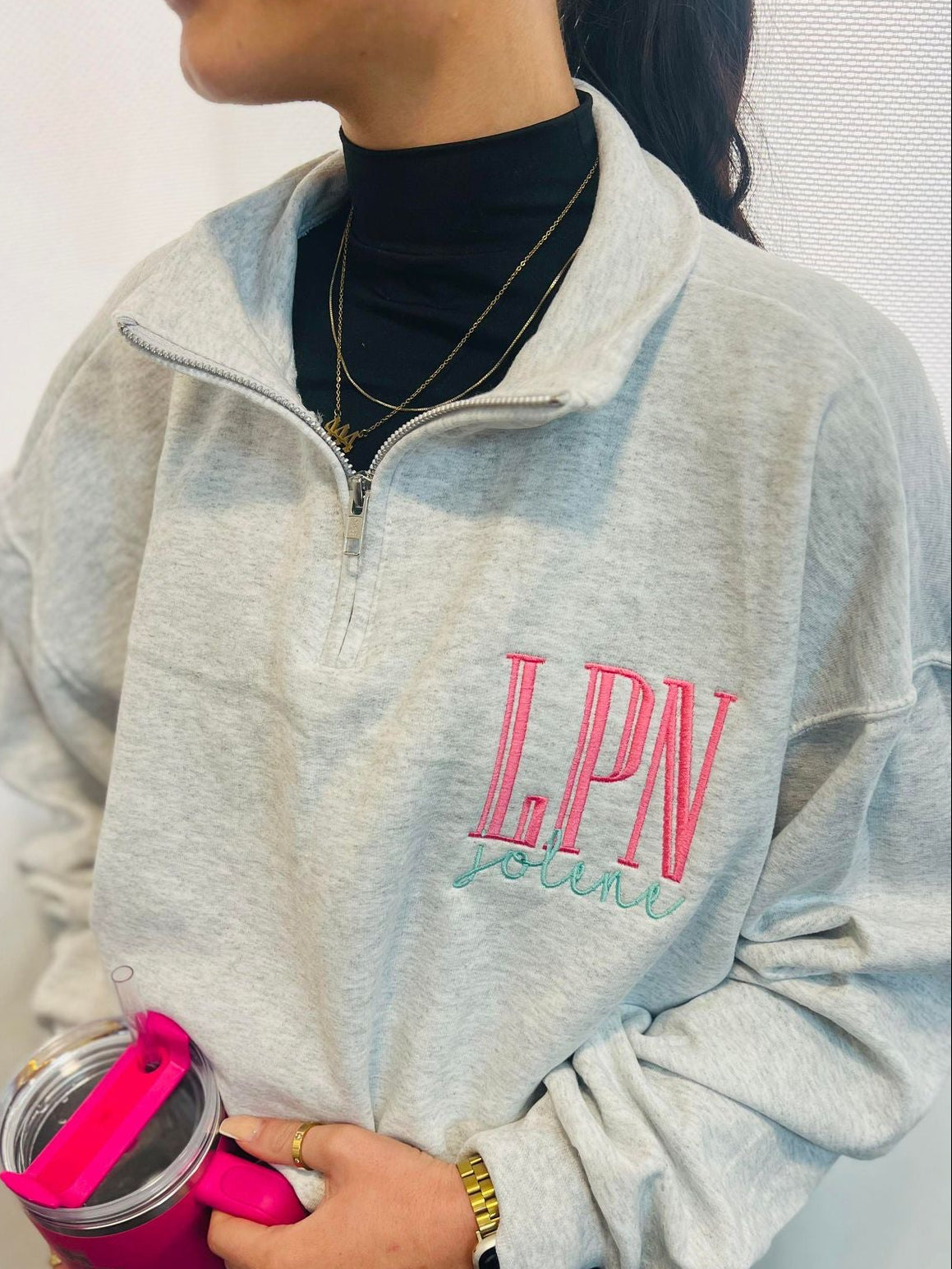 Person wearing a gray sweatshirt with 'LPN' and holding a pink water bottle.