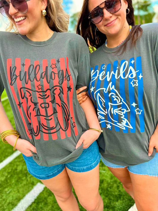 Two women wearing gray t-shirts with 'Bulldogs' and 'Devils' graphics on a grassy field.