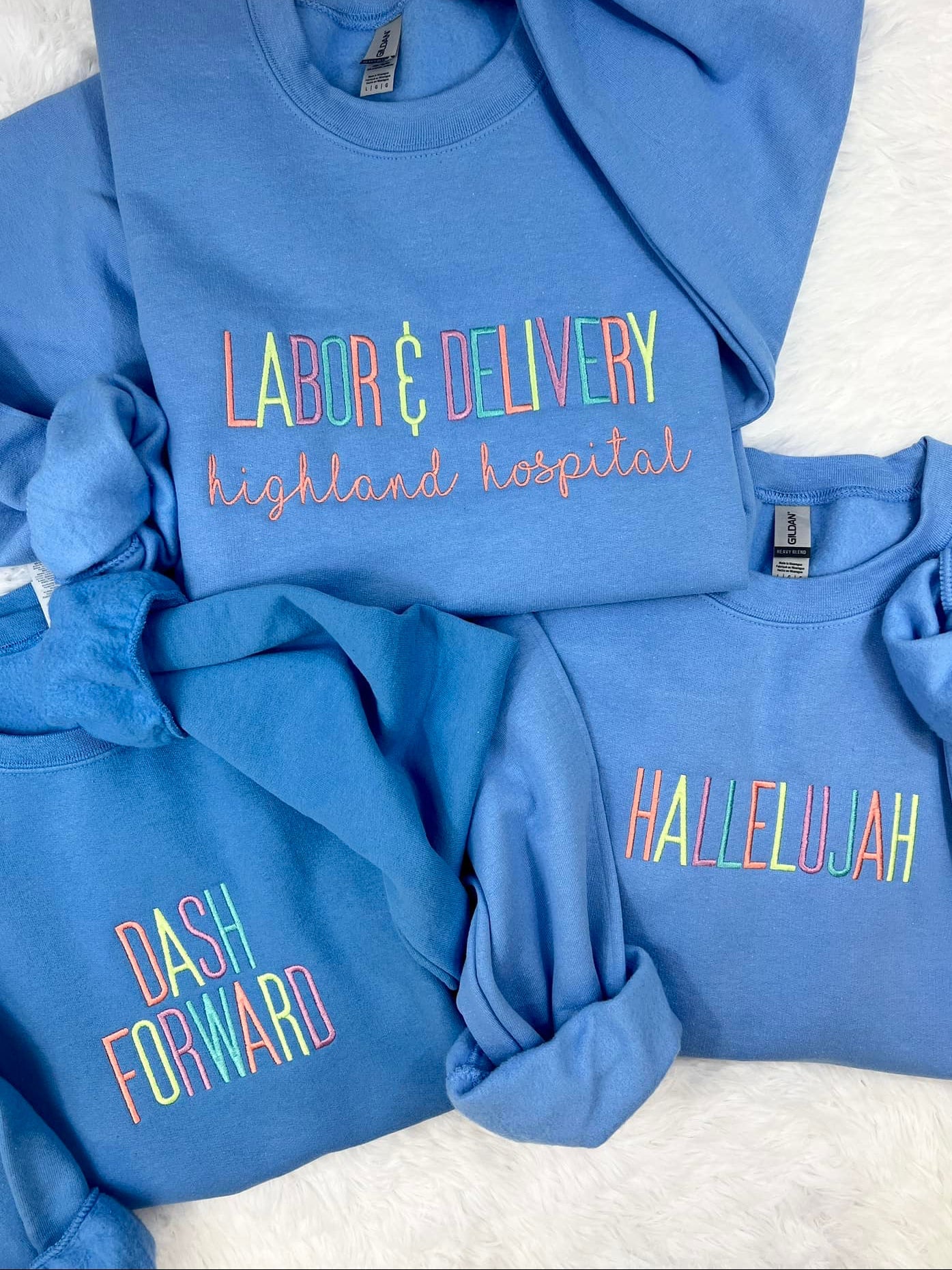 A collection of blue sweatshirts with custom embroidered text on them, like Dash Forward, displayed on a white background.