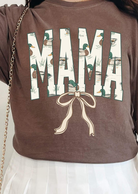 A person wearing a brown DTF tee with the word 'MAMA' and a graphic of ducks and a bow on it.