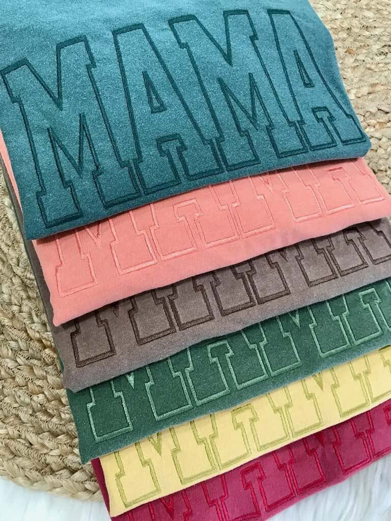 Stack of colorful fabric samples with 'MAMA' text on a textured surface