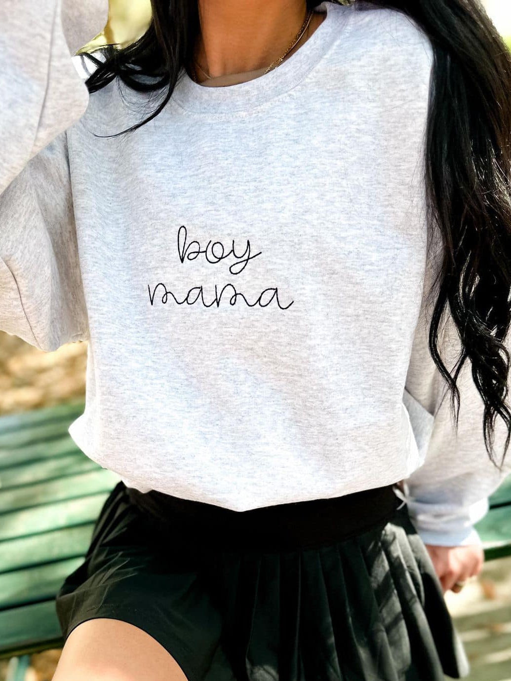 Child wearing a gray sweatshirt with 'boy mama' text, sitting on a green bench.