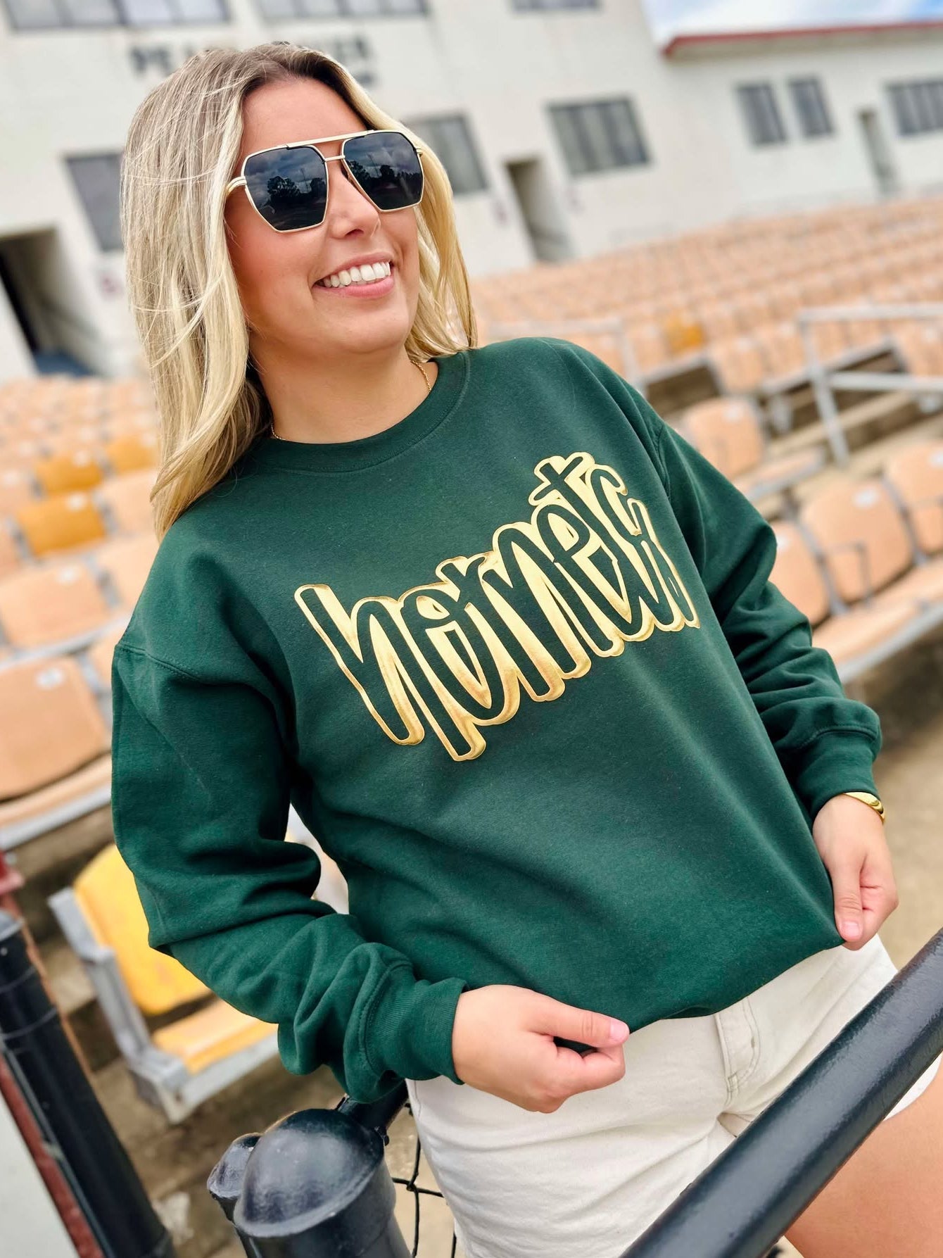 Woman wearing a green sweatshirt with 'Hornets' in gold letters, standing in an outdoor setting.