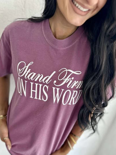 A person wearing a purple t-shirt with the text 'Stand Firm ON HIS WORD' printed in white.