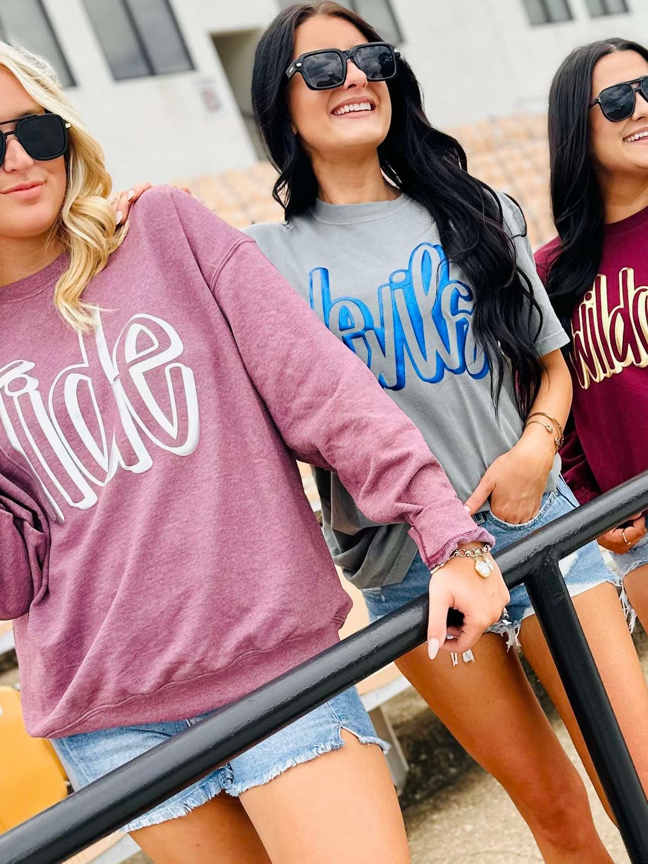 Three women wearing hoodies with 'Wilde' printed on them, standing outdoors.
