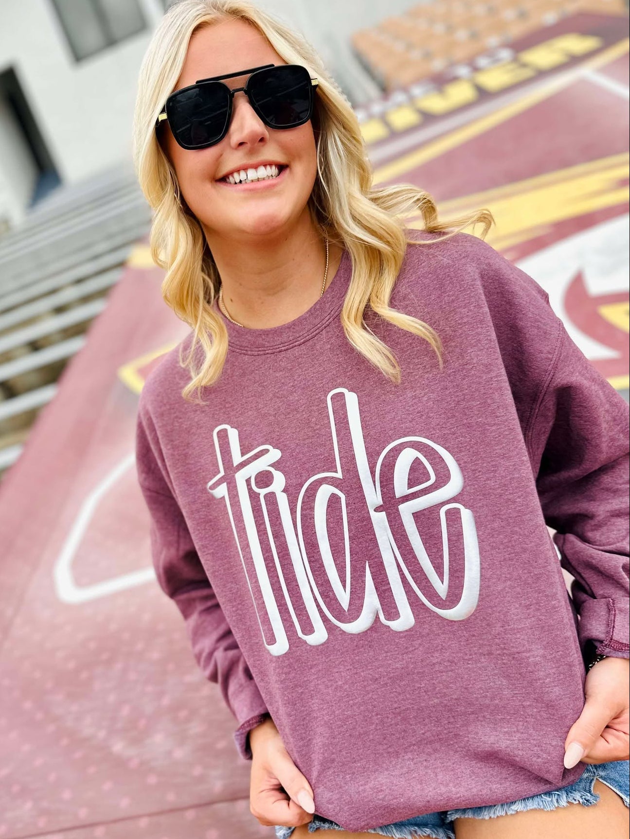 Woman wearing a purple sweatshirt with 'tide' text, standing outdoors.