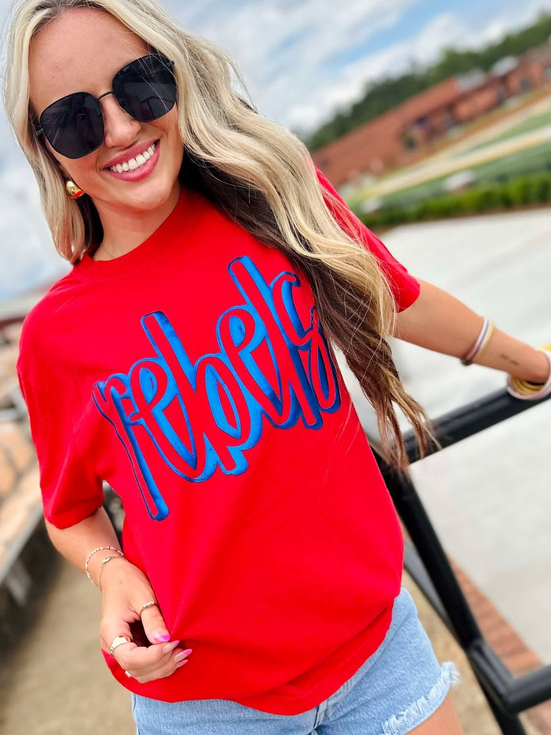 Woman wearing a red 'rebel' shirt with sunglasses outdoors.