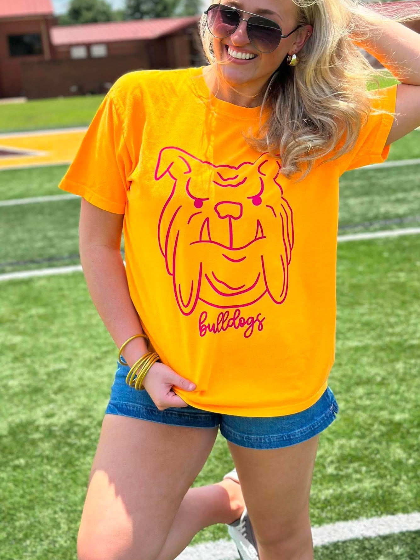 Person wearing a yellow t-shirt with a bulldog graphic on a sports field