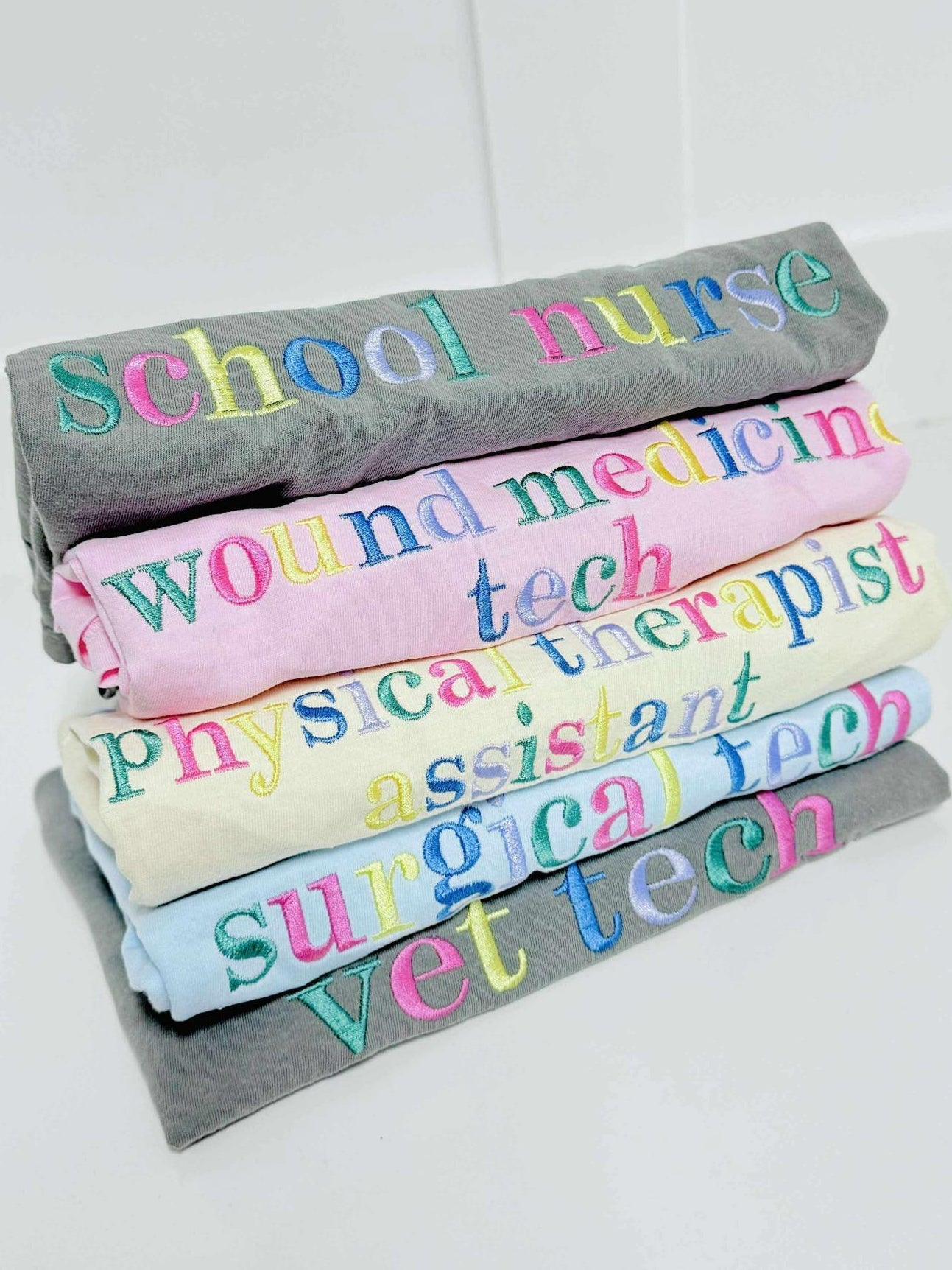 Stack of rolled-up shirts with colorful embroidery shop names on a white background