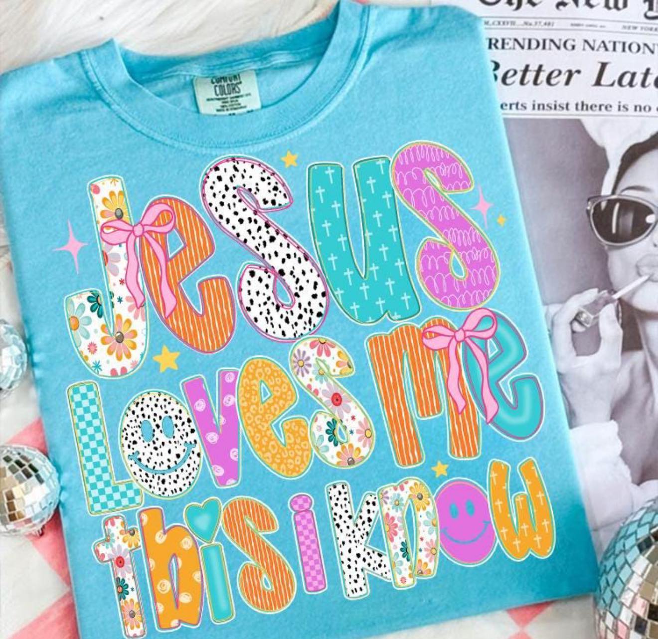 Blue t-shirt with colorful text 'Jesus loves me this I know' on a magazine background