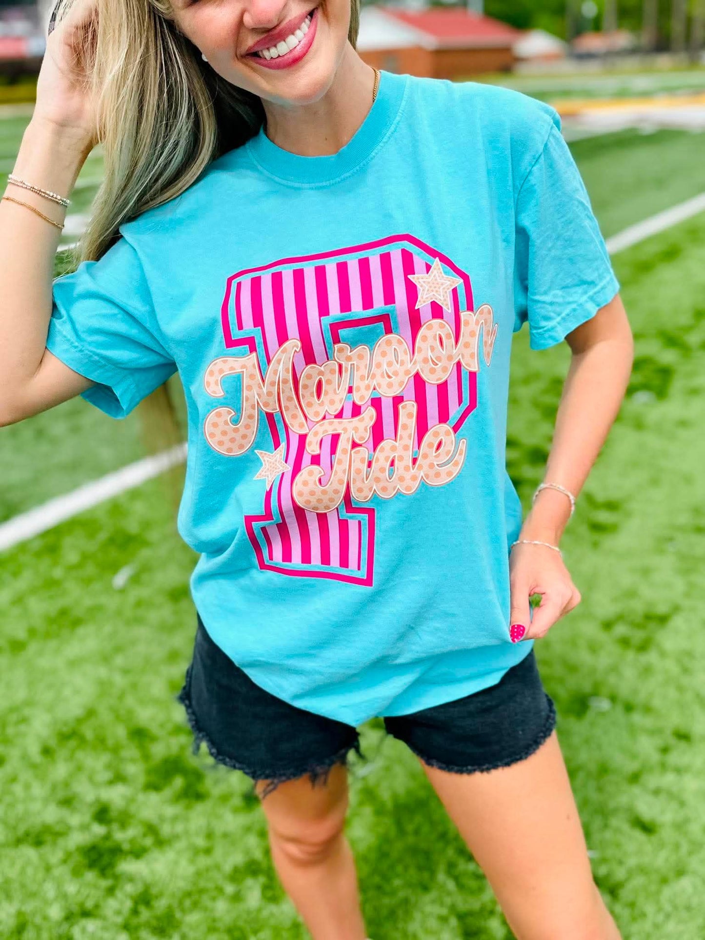 Woman wearing a blue t-shirt with a pink and white design on a grassy field