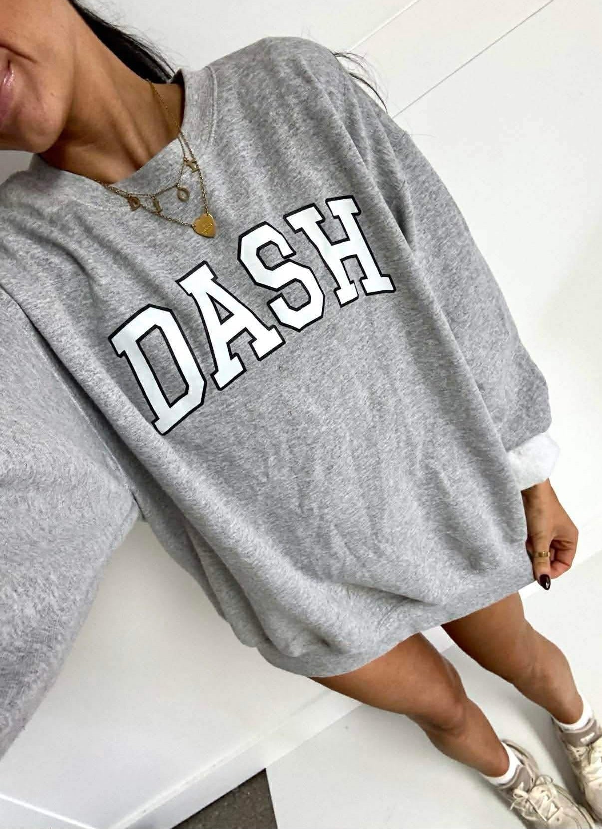 Person wearing a gray sweatshirt with 'DASH' printed on it, sitting on a white surface.