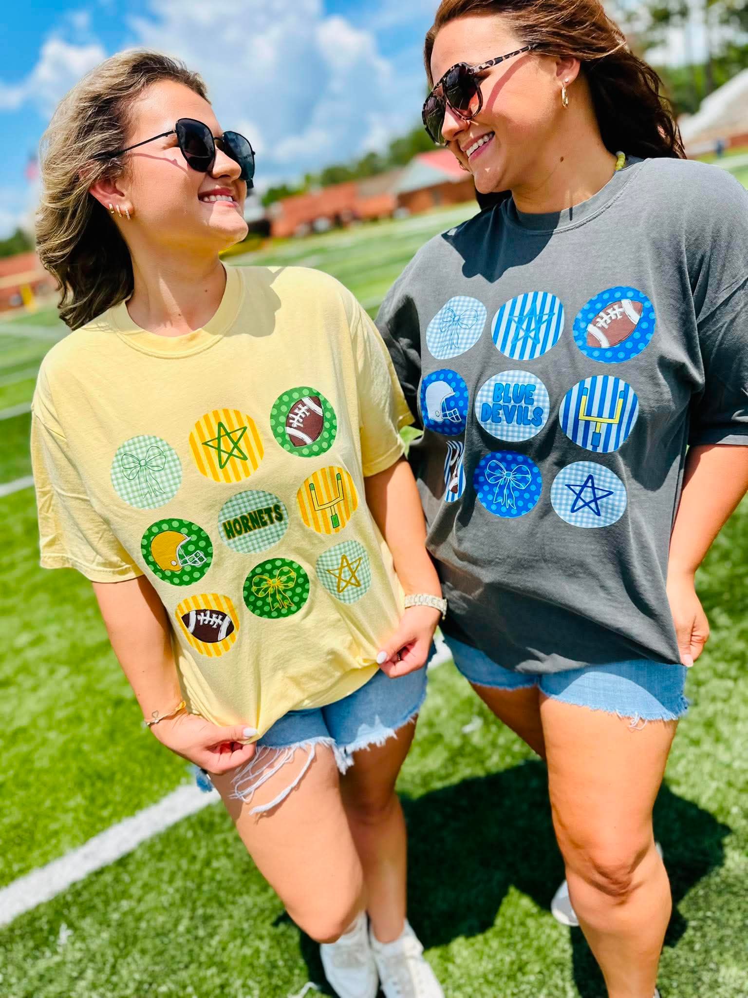 Two women standing on a grassy field wearing t-shirts with colorful circular patterns.