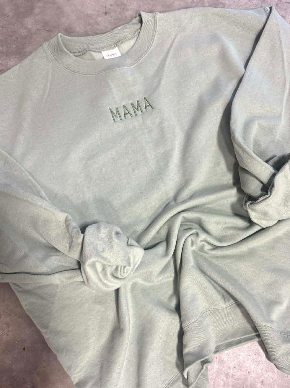 Light gray sweatshirt with 'MAMA' embroidery on a concrete floor