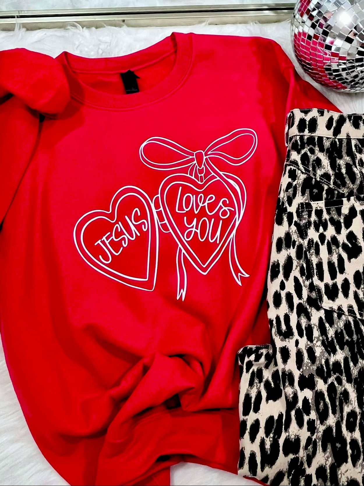 Red sweatshirt with 'I love you' design, leopard print pants, and disco balls on a white surface.