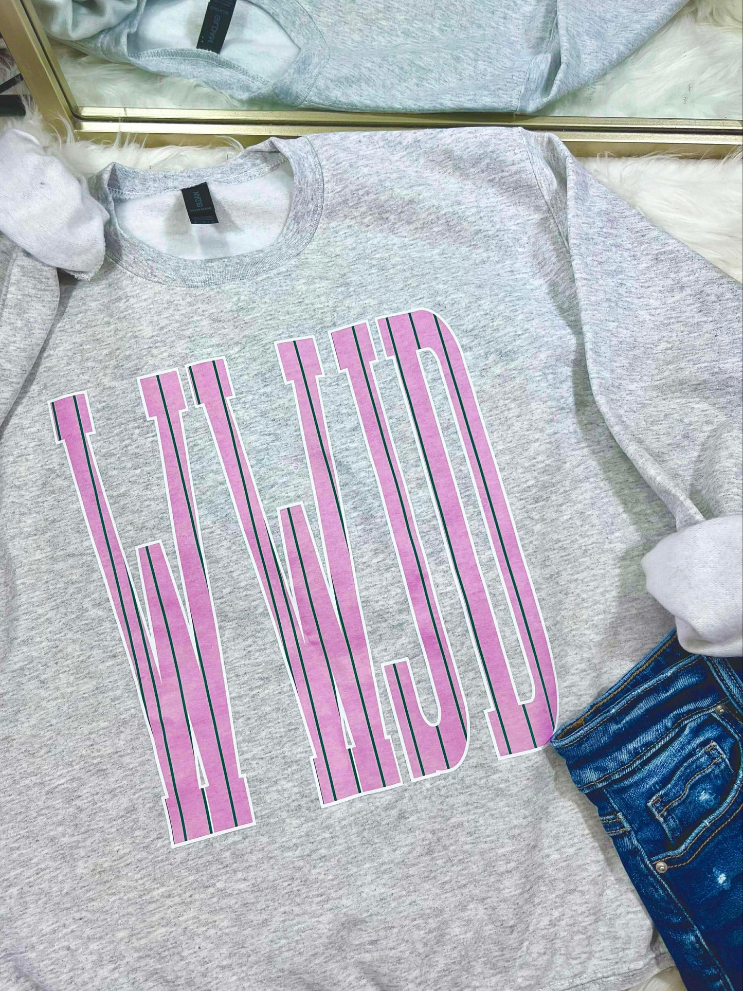 Gray sweatshirt with pink and green stripe WWJD text design on a white surface