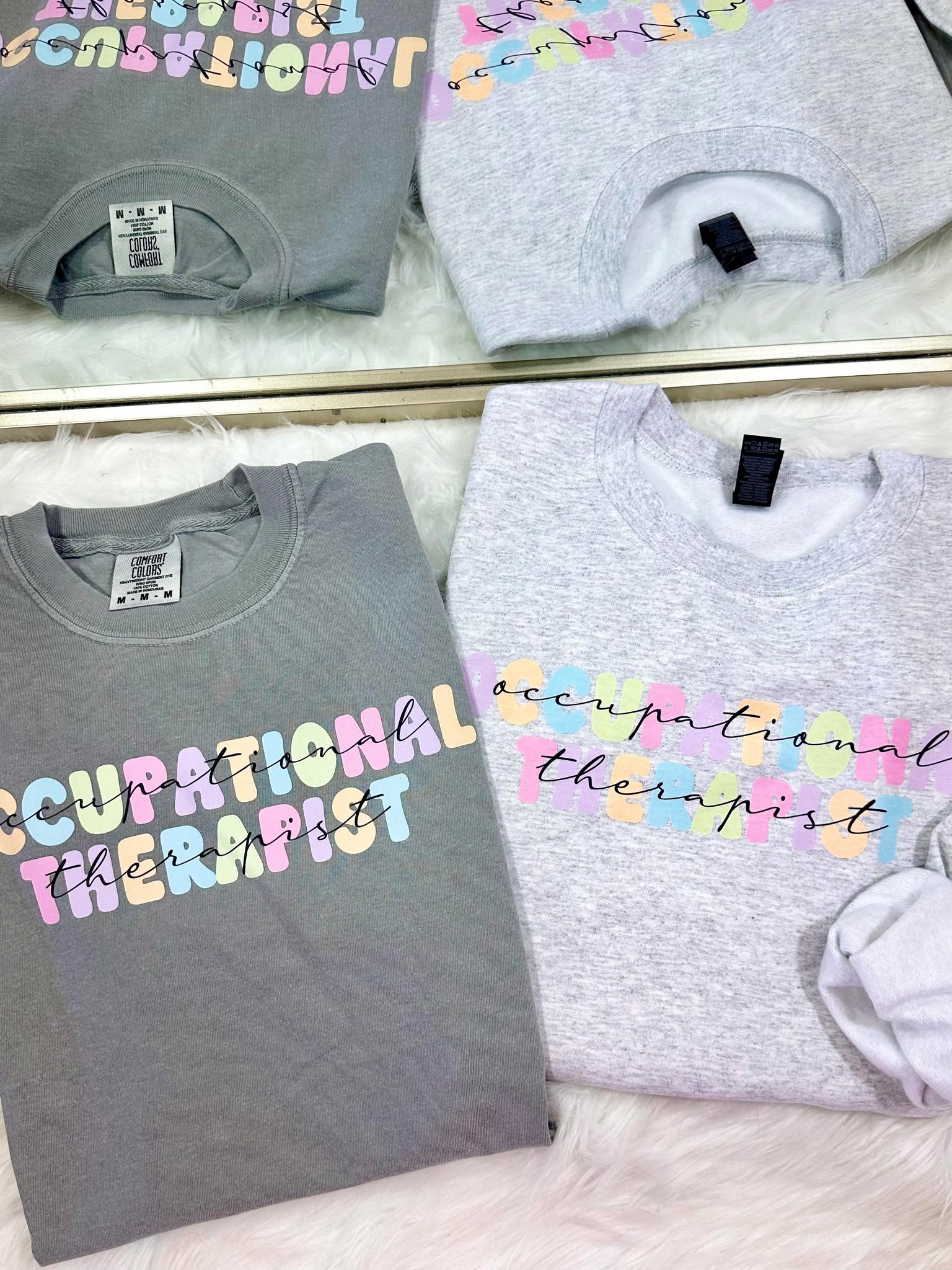 Gray t-shirts with pastel colorful 'occupational therapist' text on a mirror surface.