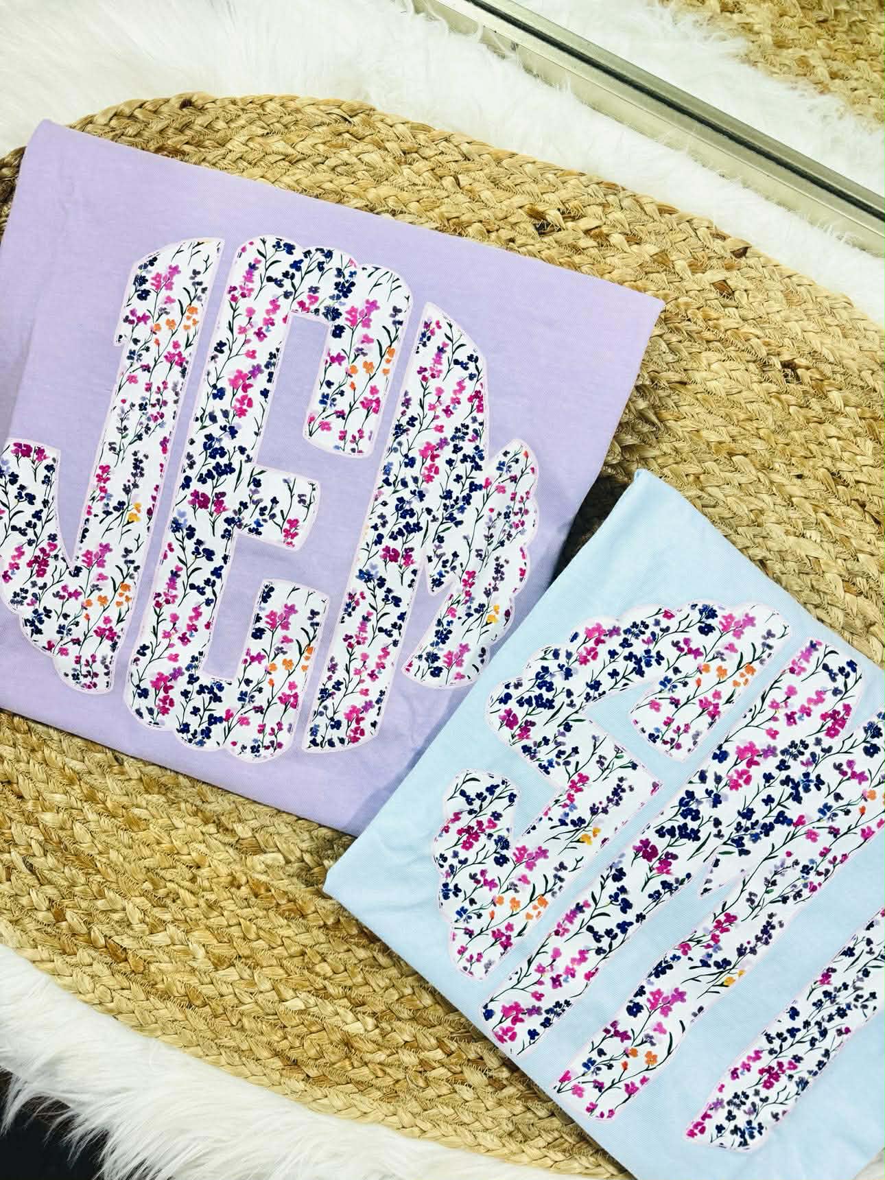 Two fabric letters, one purple and one light blue, with floral patterns on a woven surface.