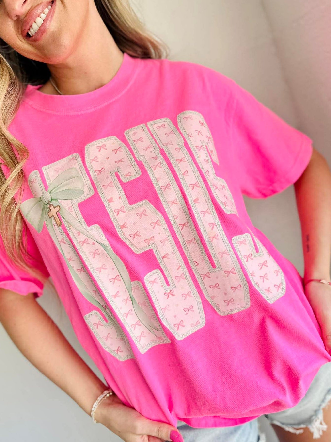 Woman wearing a pink t-shirt with decorative JESUS text with cross charm and graphics.