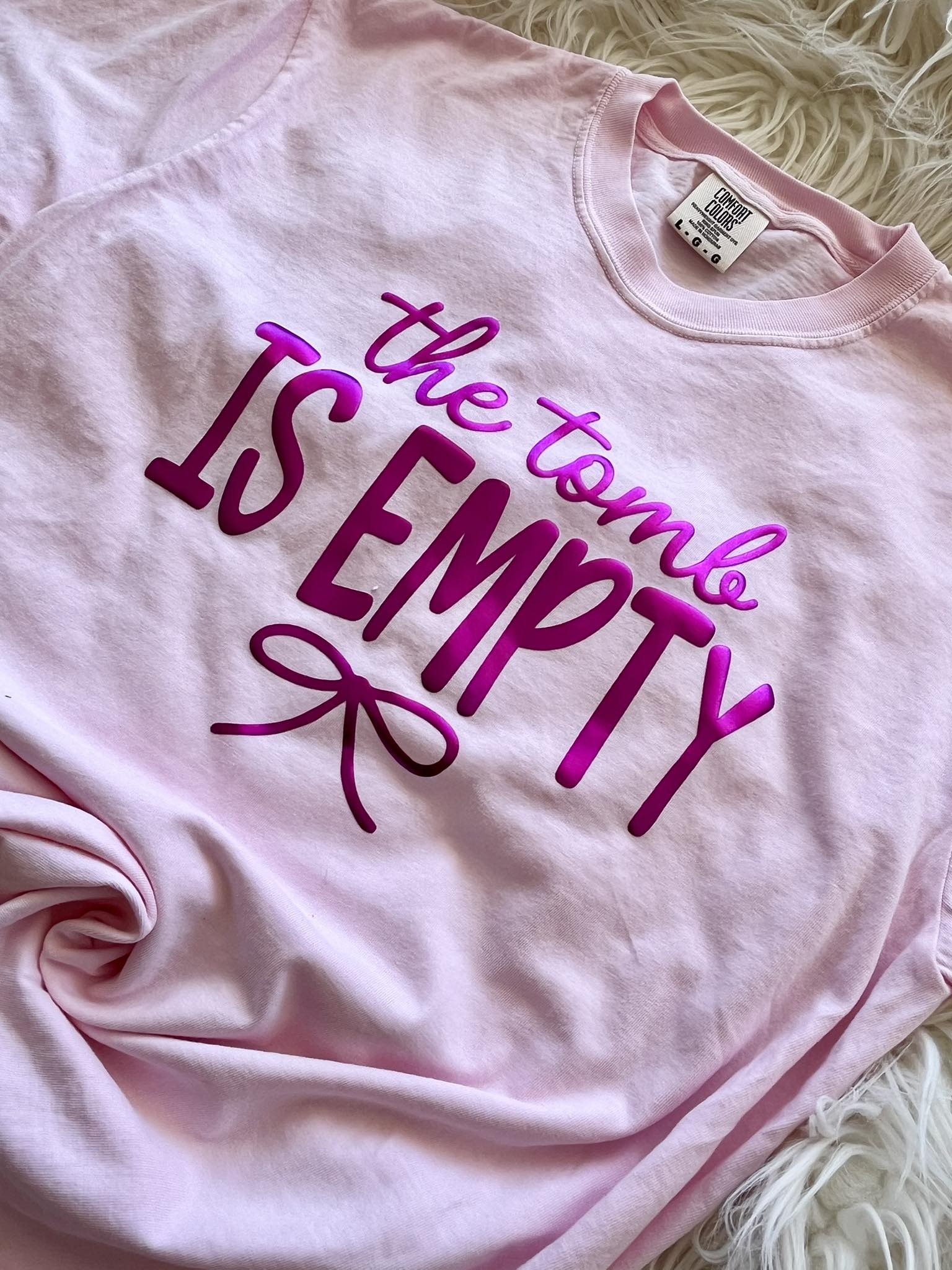 Pink t-shirt with 'the tomb is empty' text in purple on a textured surface