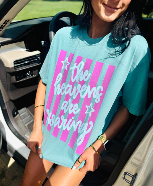 Person wearing a light blue t-shirt with pink and white text and graphics, sitting in a car.