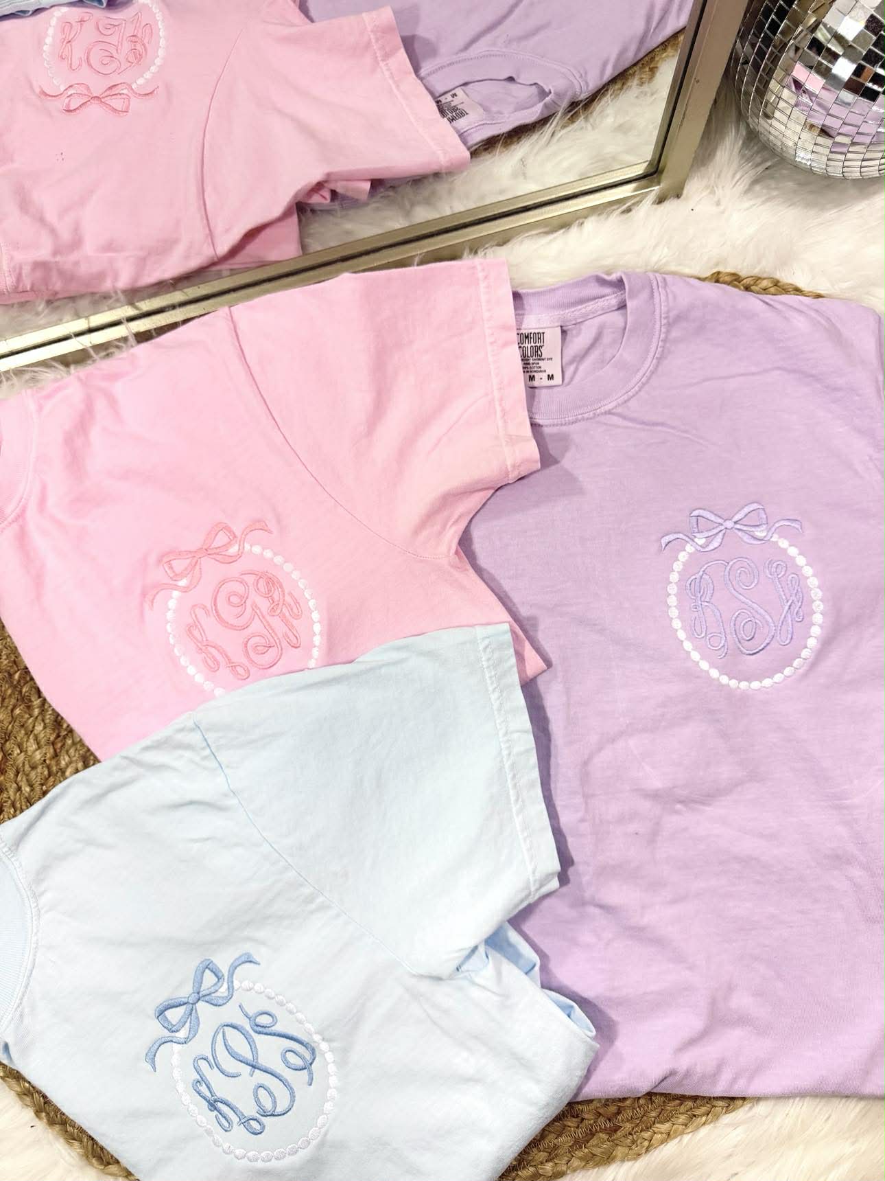 Pastel-colored shirts with embroidered designs on a textured surface.