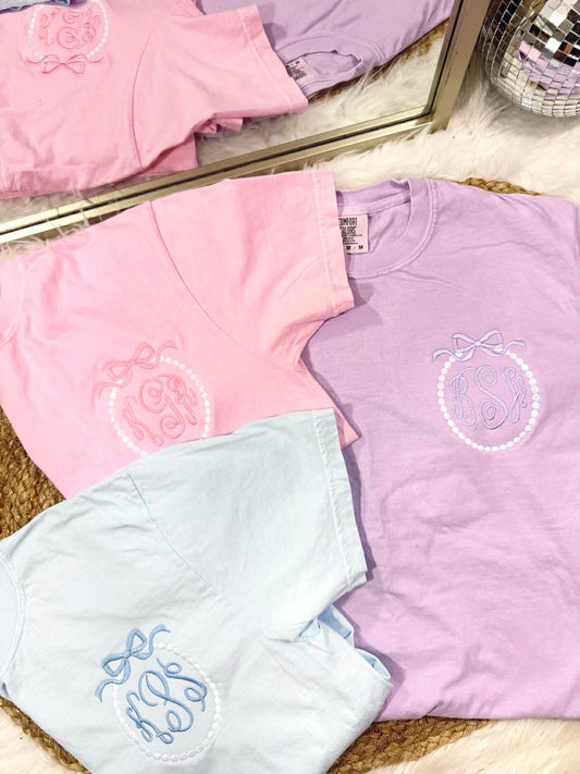 Pastel-colored shirts with embroidered designs on a textured surface.