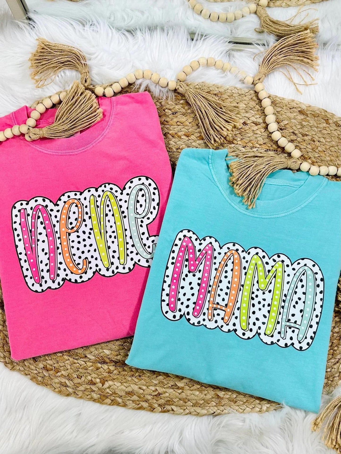 Two colorful t-shirts with 'New Mom' text on a textured surface.