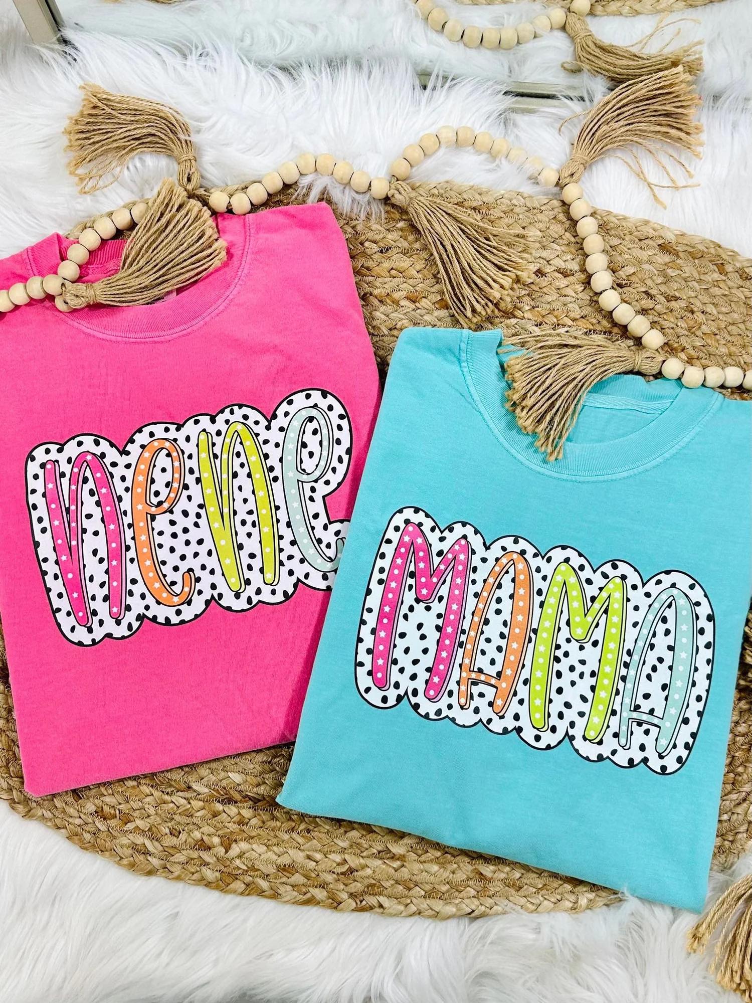 Two colorful t-shirts with 'New Mom' text on a textured surface.