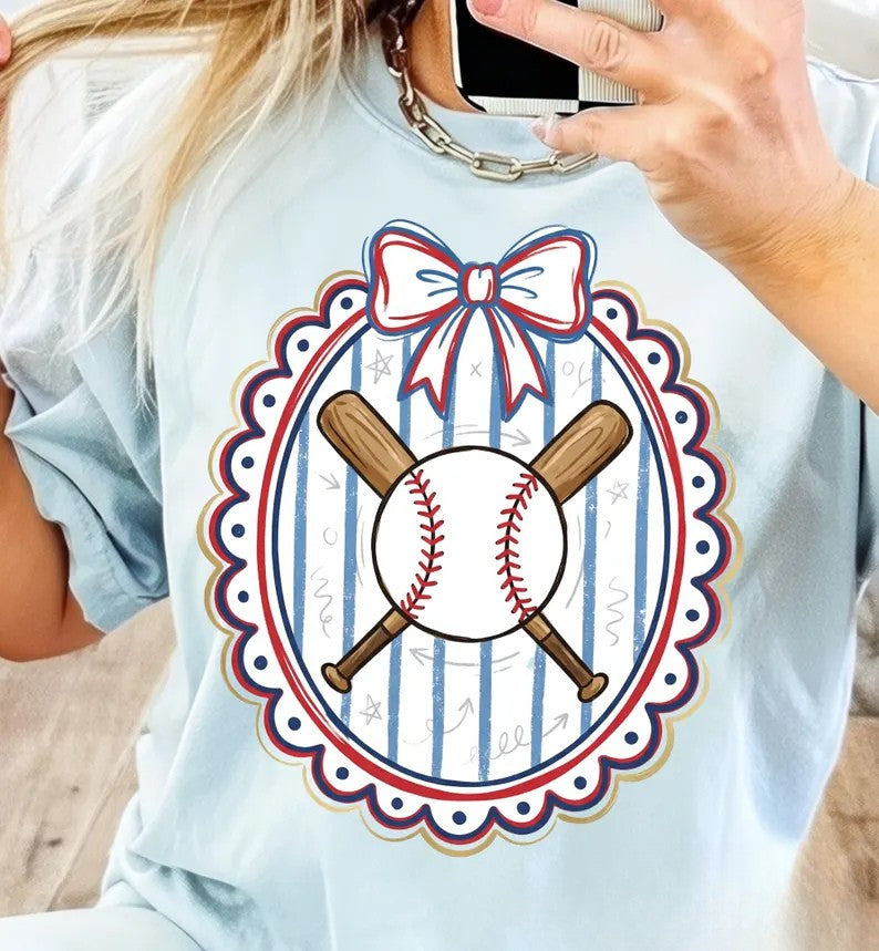 Light blue t-shirt with a graphic design of crossed baseball bats, a baseball, and a bow on a striped background.