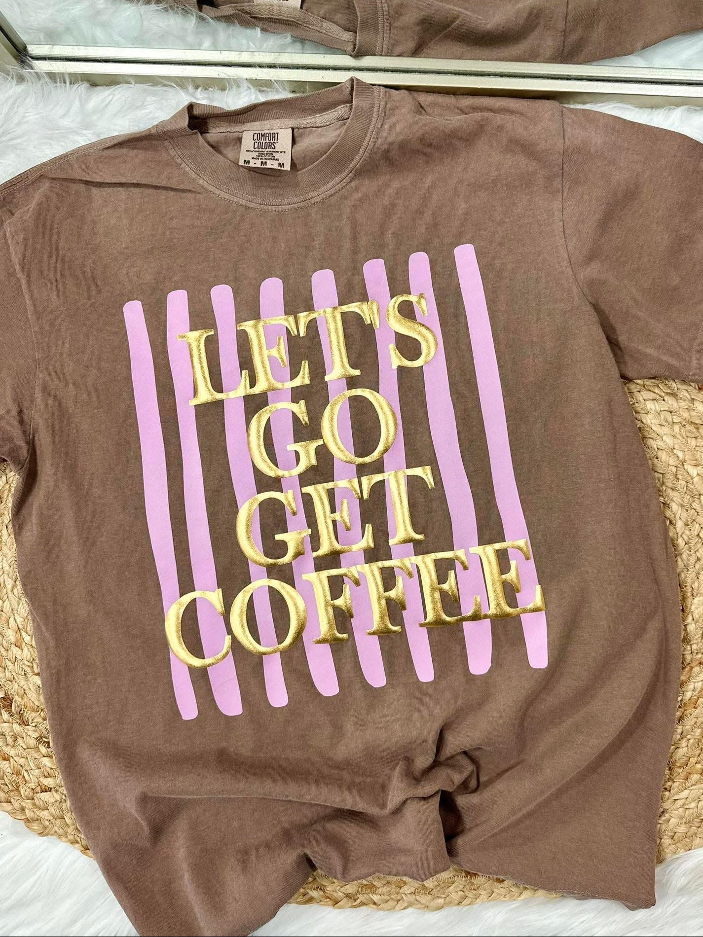Brown t-shirt with 'Let's Go Get Coffee' text on a woven surface