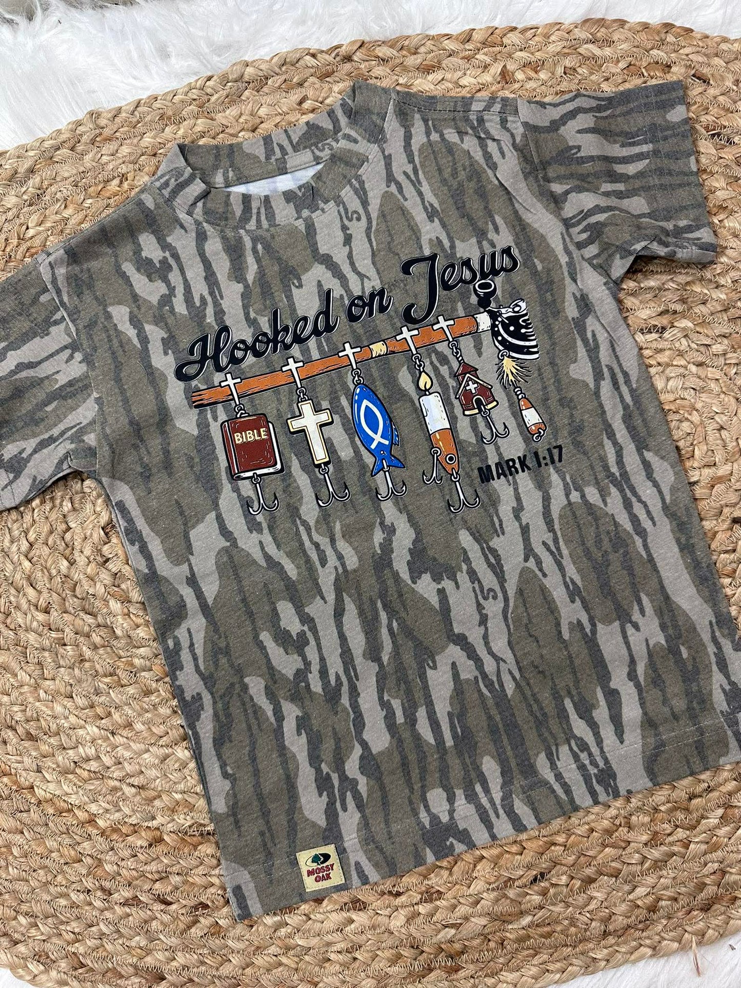 Camouflage t-shirt with fishing-themed Jesus design and text on a woven mat.