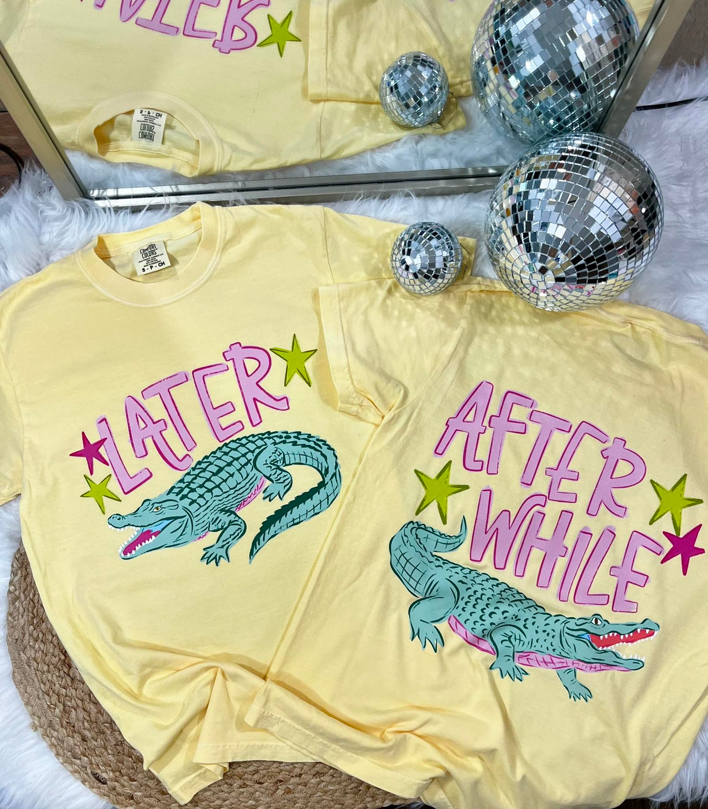 Yellow t-shirt with alligator graphic and text 'LATER' and 'AFTER WHILE' on a textured surface with disco balls.