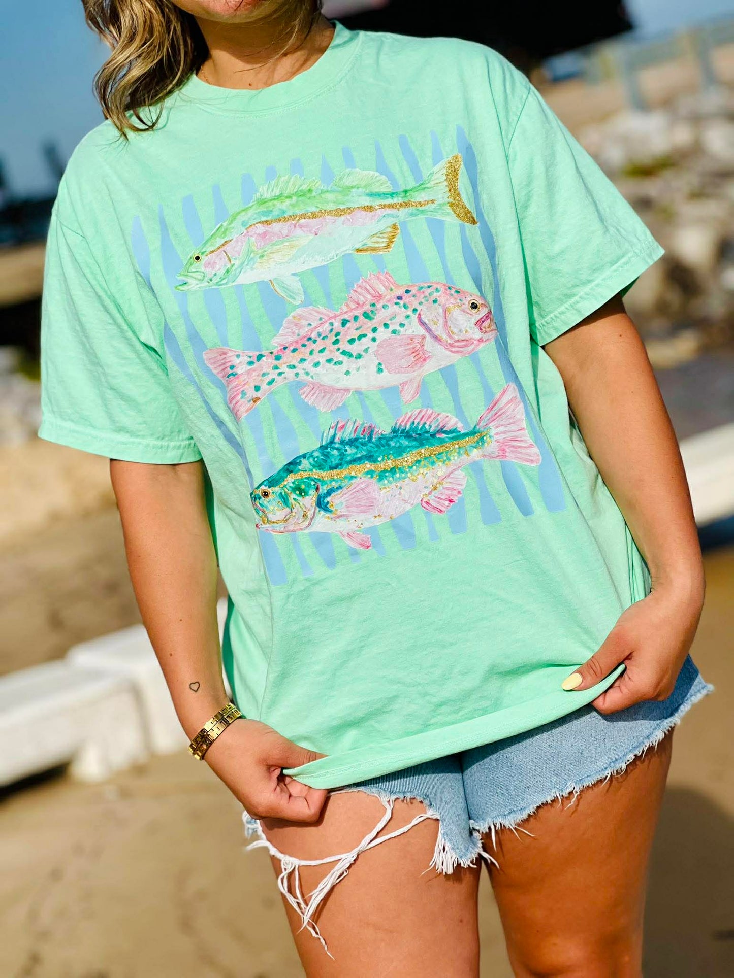 Person wearing a light green t-shirt with fish design on a beach.