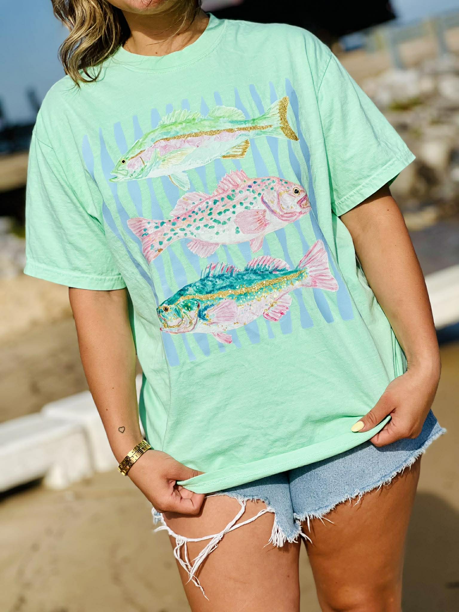 Person wearing a light green t-shirt with fish design on a beach.