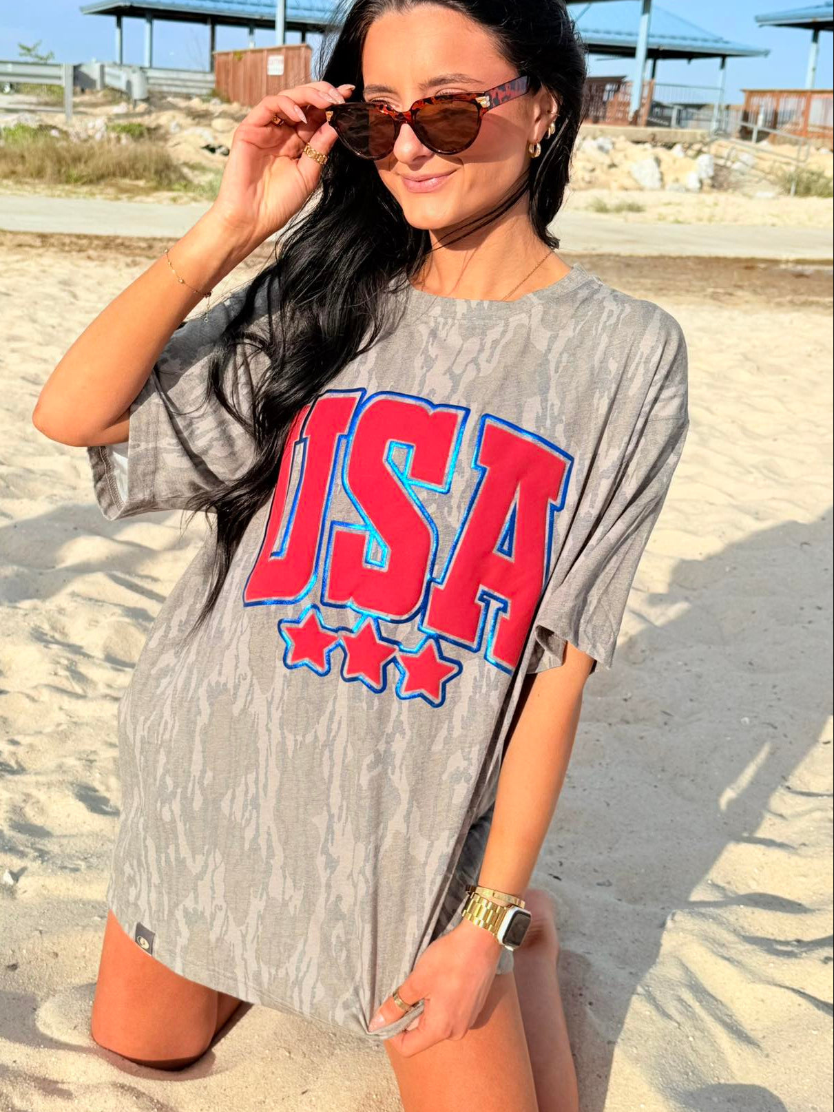 Woman wearing a bottomland 'USA' t-shirt on a sandy beach.